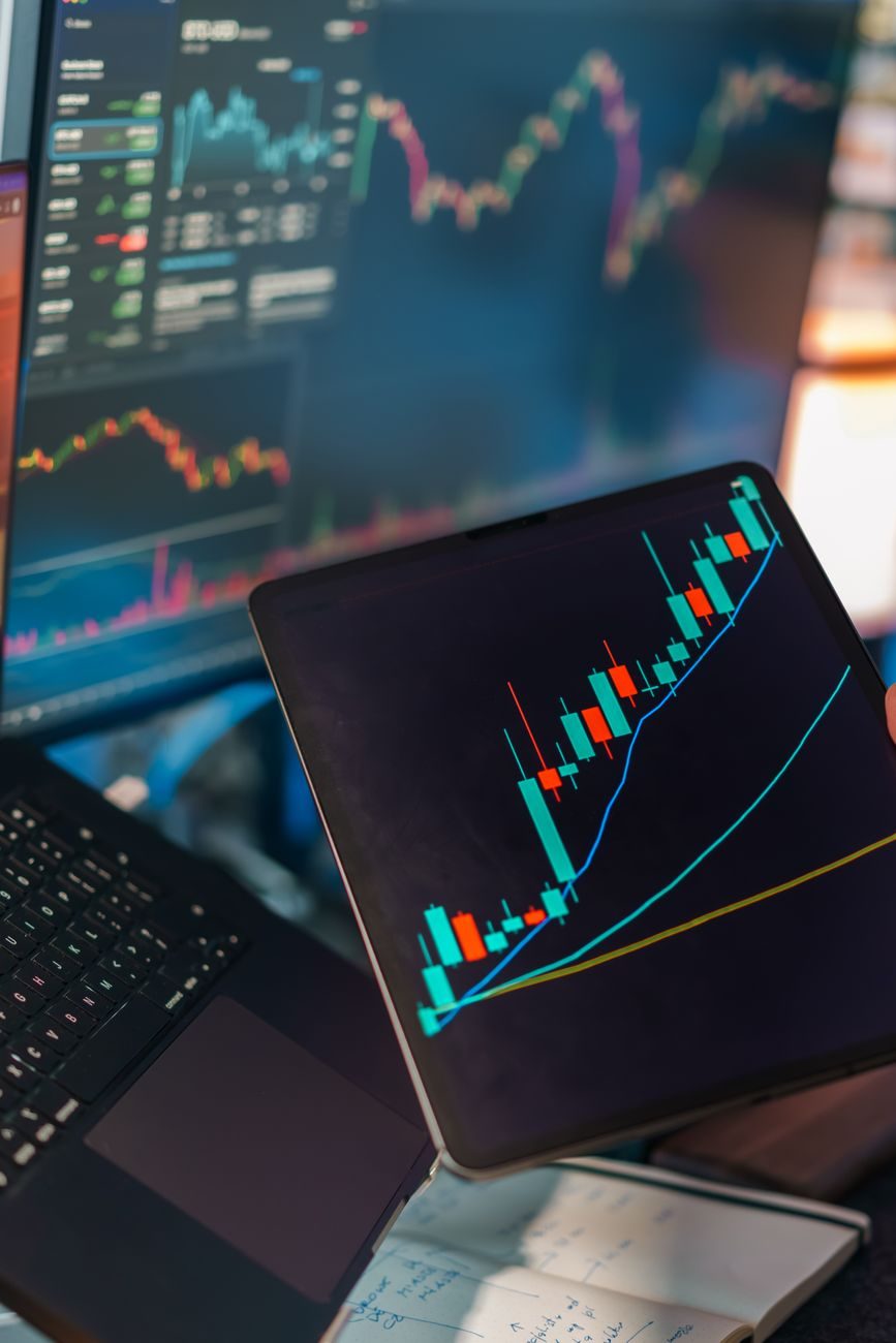 A phone displaying market charts beside a trading screen