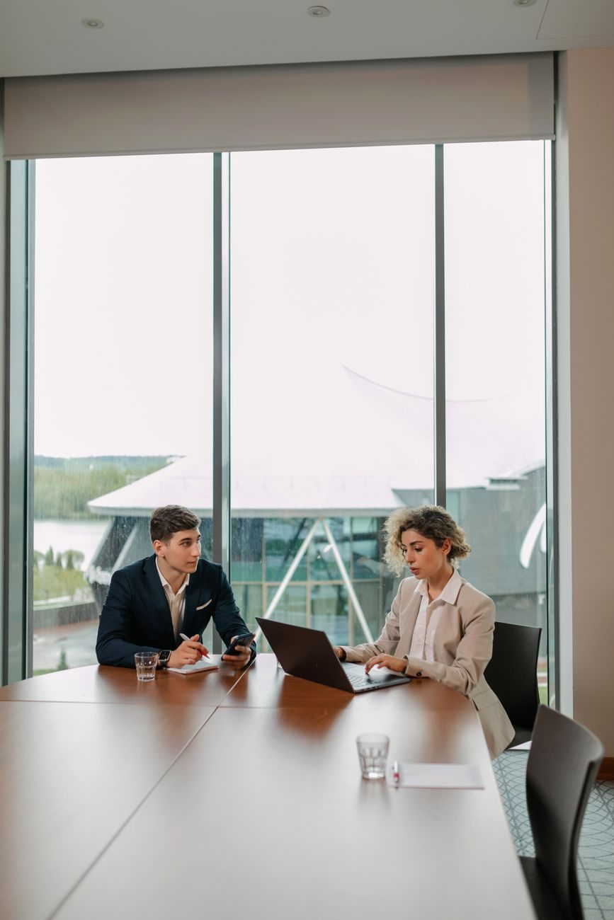 Two businesspeople reviewing work together at a glass table with a city view